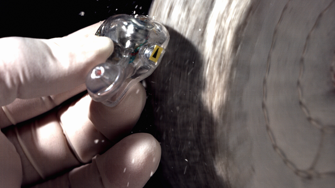 Clear plastic IEM shell held by a gloved hand being polished against a dark background