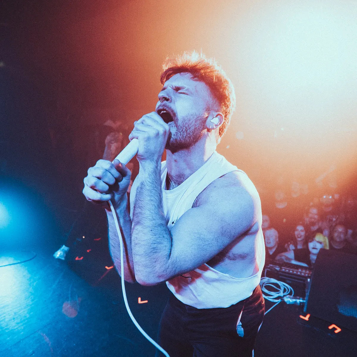 CITYISOURS vocalist in a white graphic tank top sings into a microphone with the crowd behind him.