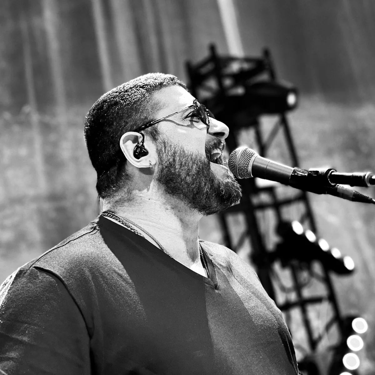 Steve Maggiora sings into a microphone in glasses and in-ear monitors, photographed in black and white.