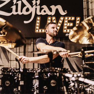 Man playing drums with Zildjian cymbals and logo in the background