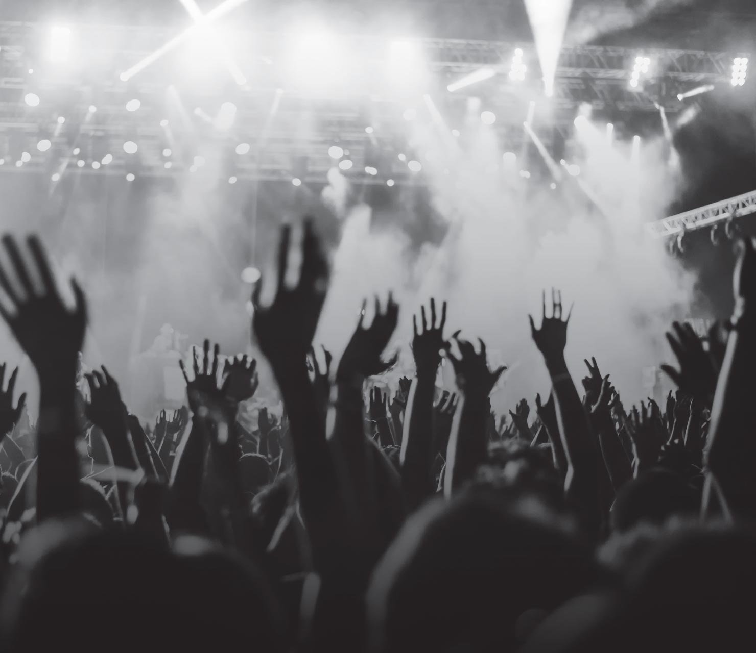 A crowd of people dancing at a live show with their hands in the air in black and white.