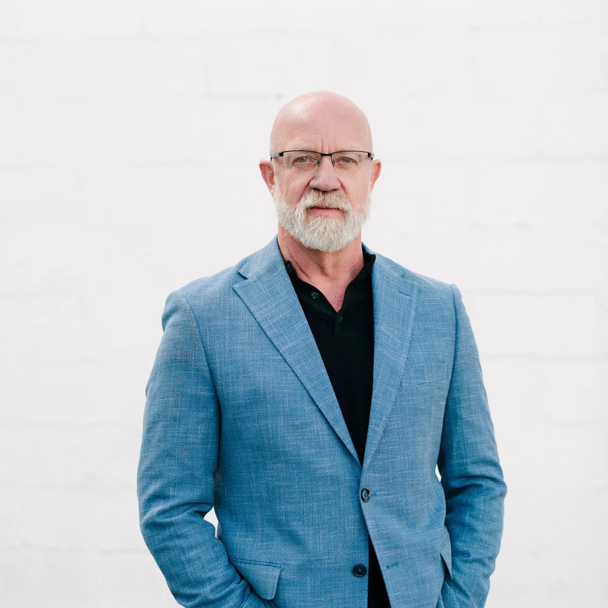 Dave Stroud in a blue jacket and glasses against a white wall.