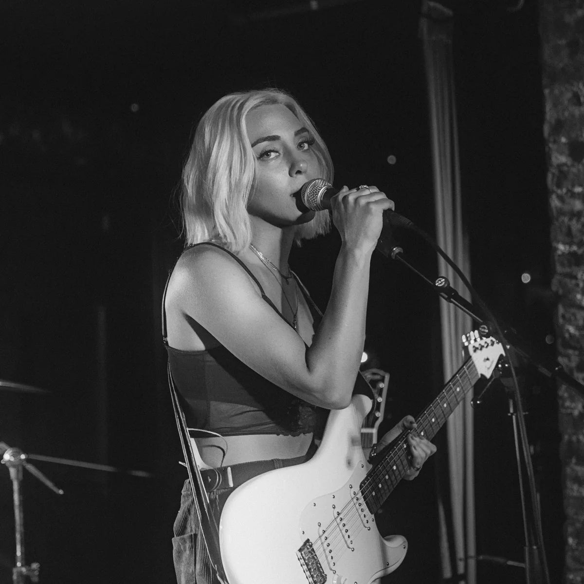Destiny Petrel holds a microphone near her mouth with an electric guitar across her body, photographed in black and white.