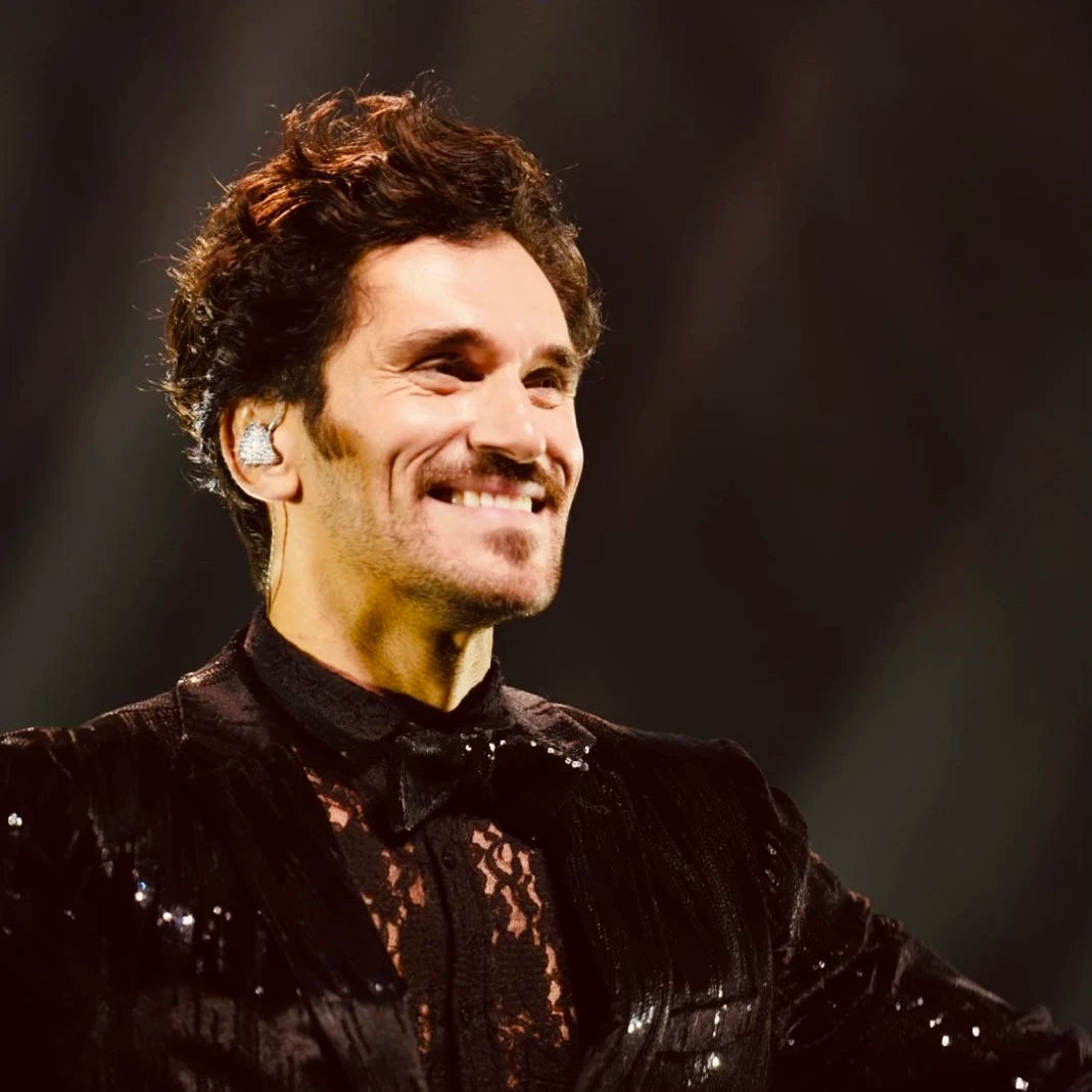 Close-up of Vladimir Korneev smiling onstage in a black jacket and in-ear monitors.
